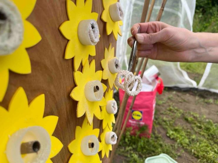 Adding a string containing pollen to the artificial flowers. The string is being placed on a pipe that is surrounded by a plastic ring. A flower shape is around each ring.